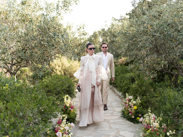 Wedding guests walking through olive grove to chapel ceremony at Paros destination wedding.