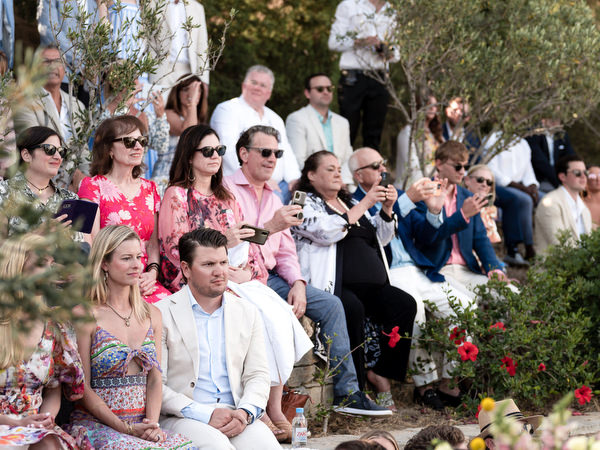 Wedding guests seated under olive trees at Petra Farm Orthodox ceremony in Paros.
