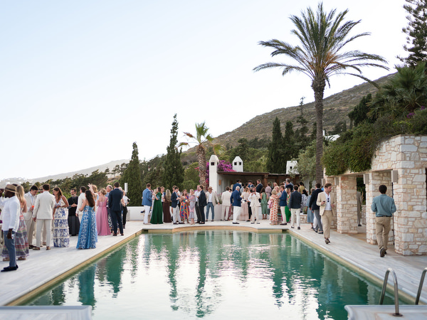 Guests mingling by swimming pool during cocktail hour at Petra Farm wedding in Paros.