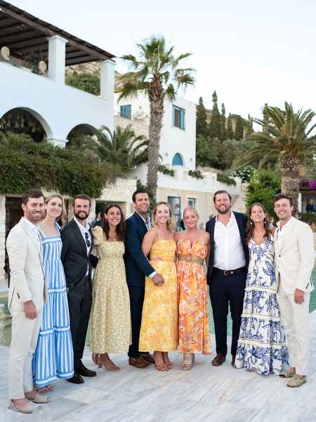 Group of wedding guests posing at Petra Farm with Paros landscape in background.