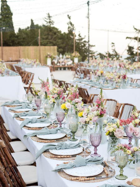 Long wooden banquet tables with floral centerpieces at Petra Farm wedding in Paros.