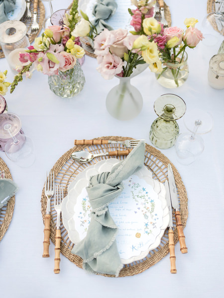 Greek island wedding table setting with woven placemats and pastel napkins.