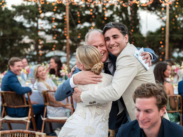 Father hugging bride and groom during outdoor wedding reception in Paros Greece.