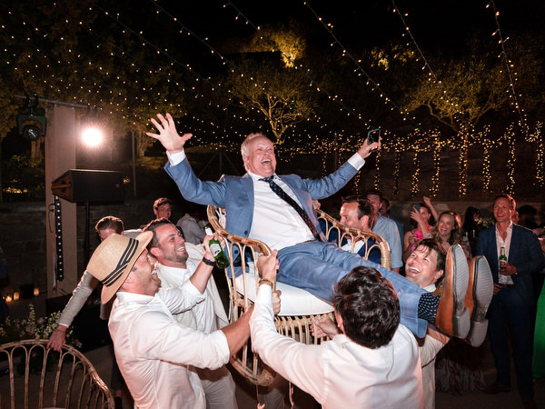 Wedding guest lifted on chair during Greek island wedding party in Paros.