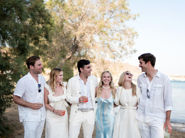 Guests chatting while posing during beachside wedding welcome event in Paros