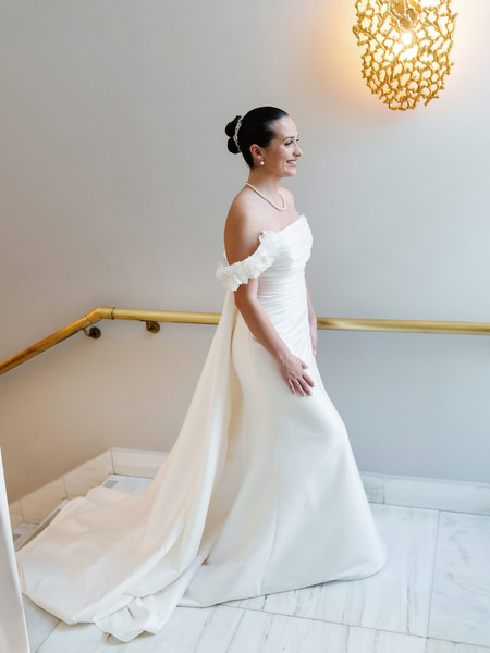 Bride walking down staircase in elegant gown before Catholic ceremony in Athens Greece.