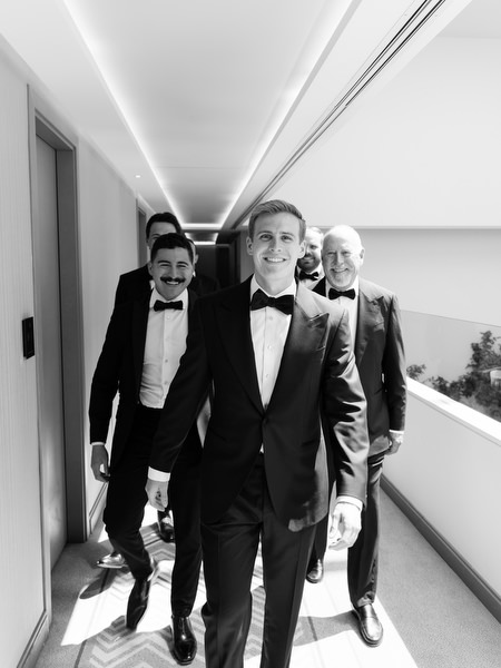 Groom and groomsmen walking down hotel corridor before Athens Catholic church wedding.
