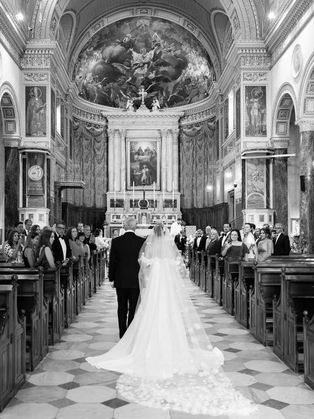 Black and white image of bride walking down cathedral aisle during Athens Catholic wedding ceremony.