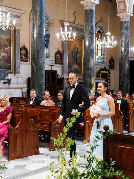 Bridal party walking down aisle inside grand historic Catholic church in Athens Greece.