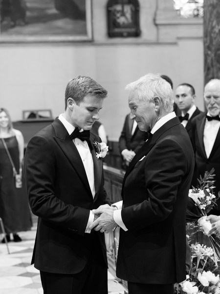 Emotional handshake between groom and bride’s father during Catholic wedding ceremony in Athens.