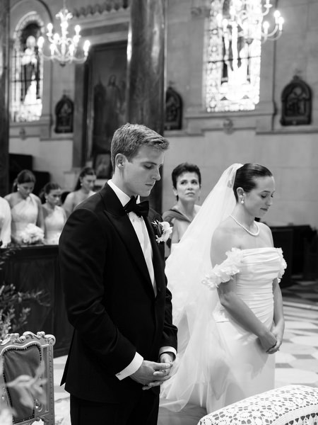 Bride and groom bowing heads in prayer during Catholic wedding ceremony in Athens cathedral.