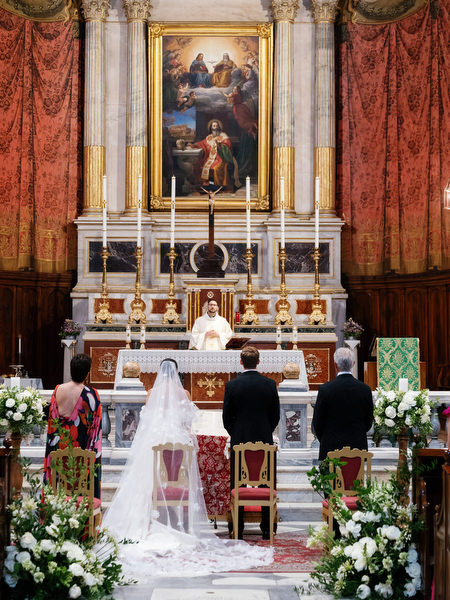 Bride and groom standing before ornate altar during grand Catholic wedding ceremony in Athens.