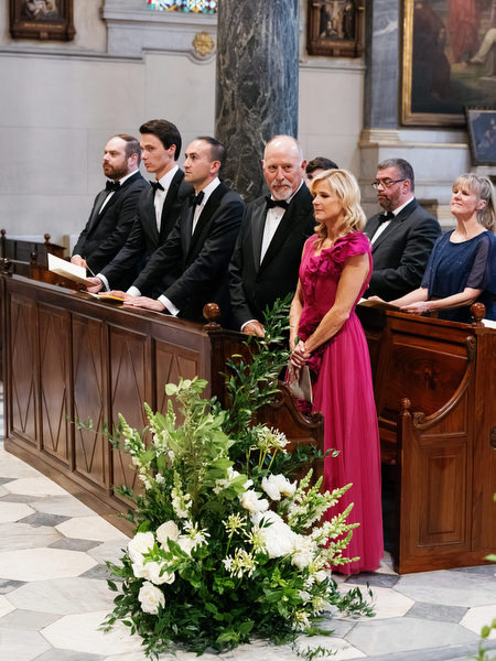 Family members standing during Catholic wedding ceremony inside historic Athens church.