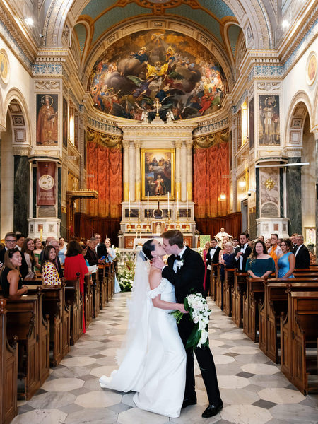 Bride and groom sharing first kiss inside ornate Catholic church during luxury Athens wedding.
