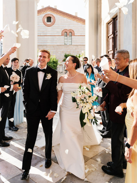 Newlyweds walking through cheering guests outside Athens cathedral after Catholic wedding ceremony.