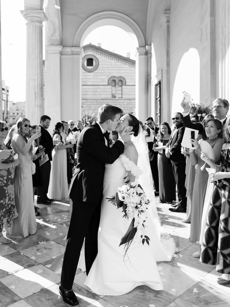 Bride and groom kissing outside grand Catholic church in Athens after ceremony exit.