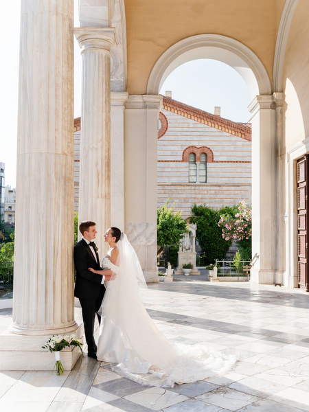 Bride and groom embracing under sunlit arches in Athens before Island Resort Riviera wedding reception.