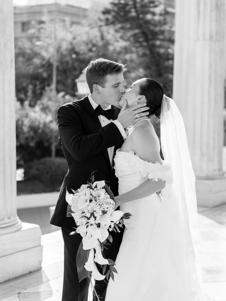 Bride and groom sharing romantic kiss under classical columns in Athens Greece after church ceremony.