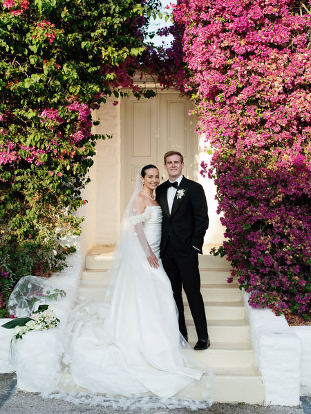 Bride and groom posing beneath blooming bougainvillea at The Residence Island Resort Athens.