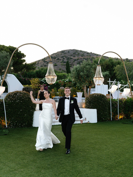 Bride and groom entering outdoor reception under chandeliers at Island Resort Athens Riviera.