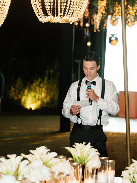 Groomsman giving speech under glowing chandeliers at The Residence Island Resort Athens Riviera.