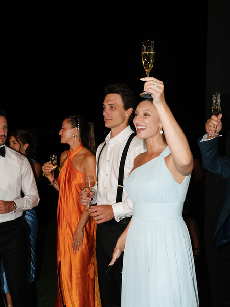 Wedding guests raising champagne glasses during evening reception at Island Resort Athens Riviera.