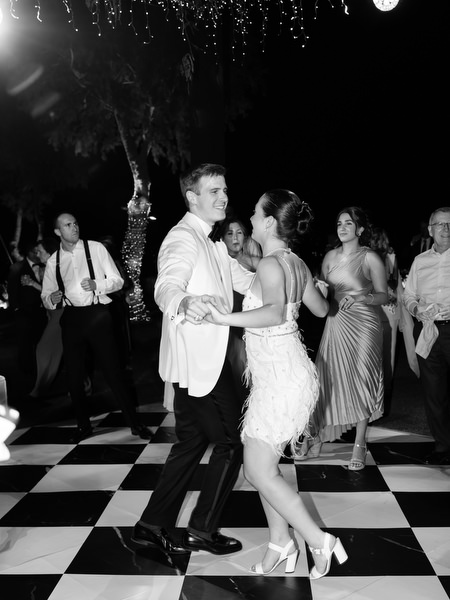 Bride in feather party dress dancing with groom on checkered dance floor at Athens Riviera wedding.