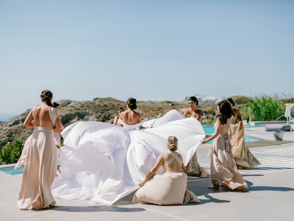 Bridesmaids arranging dramatic wedding dress in Santorini.