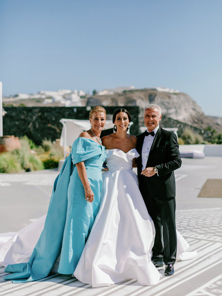 Bride with parents overlooking Santorini caldera.