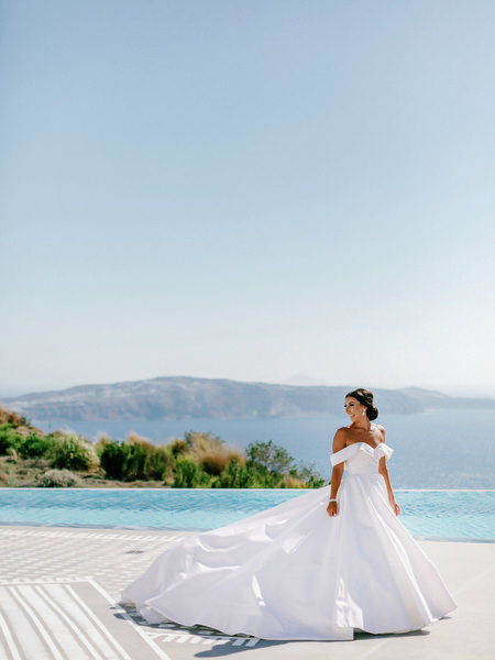 Bride in couture gown overlooking Santorini caldera.