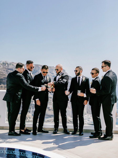 Groomsmen toast overlooking Santorini caldera.