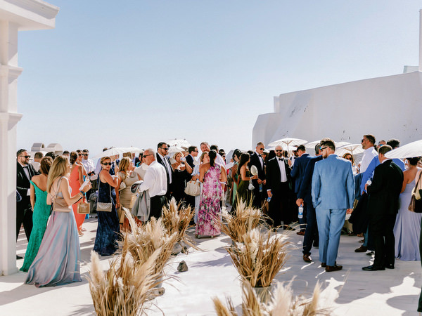 Wedding guests gathering on Santorini terrace with caldera views.