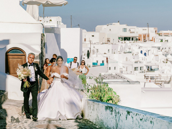 Bride walking through Santorini village streets with father.