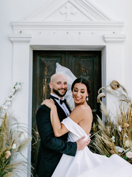 Bride and groom embracing outside white chapel.