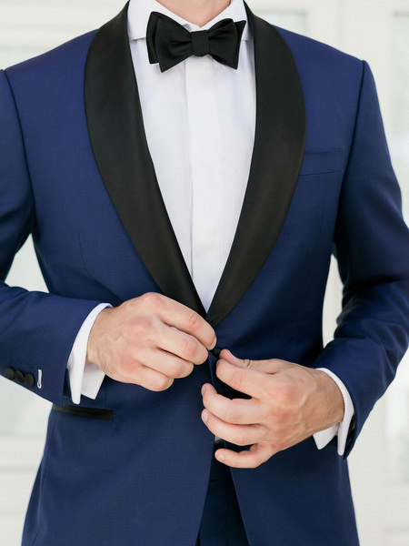 Groom adjusting navy tuxedo before Santorini wedding at Venetsanos Winery.