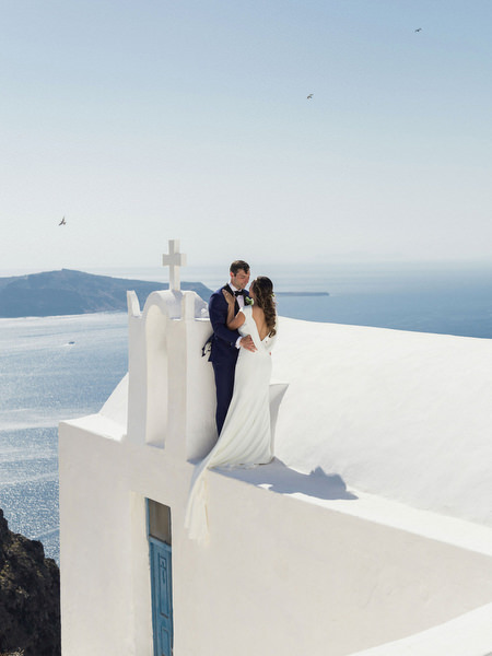 Bride and groom on Santorini chapel rooftop before Venetsanos Winery wedding.