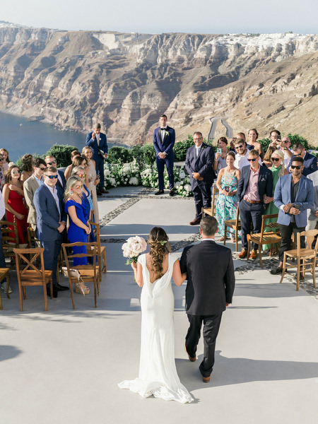Bride walking down aisle at Venetsanos Winery overlooking Santorini caldera.