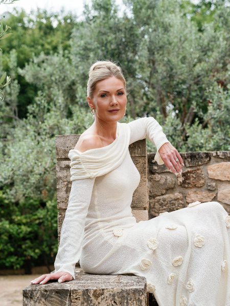 Bride seated outdoors in her wedding gown surrounded by olive trees and greenery