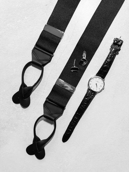 Black and white flat lay of the groom’s suspenders, bow tie and wedding accessories