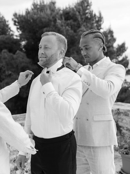 Black and white photo of a groomsman adjusting the groom’s bow tie