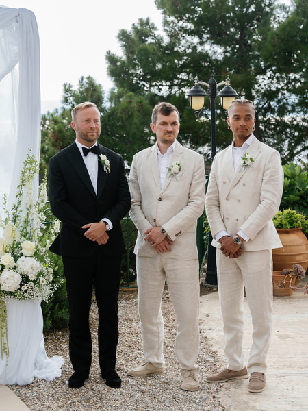 Groom standing with his groomsmen beside the floral ceremony setup at Pyrgos Ralli
