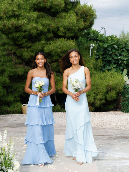 Two bridesmaids in blue dresses posing with white floral bouquets in Aegina