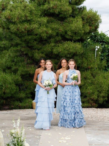 Bridesmaids in blue dresses posing with white floral bouquets in Aegina