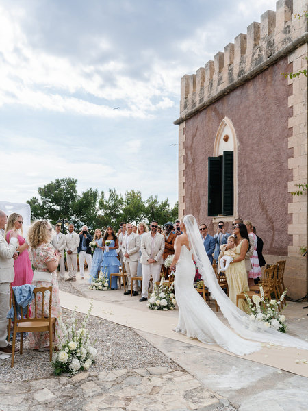 Bride walking down the aisle beside the historic tower at Pyrgos Ralli in Aegina