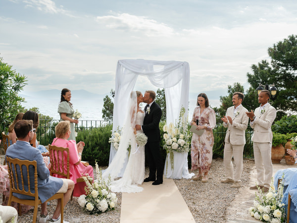 Newlyweds kissing beneath the ceremony arch after exchanging vows at Pyrgos Ralli