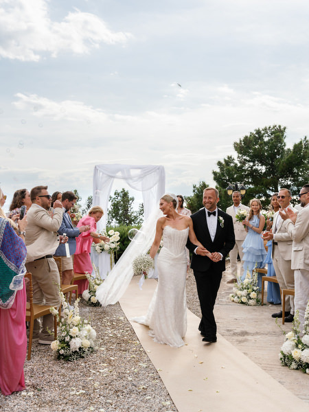 Newlyweds walking back down the aisle as guests cheer at Pyrgos Ralli