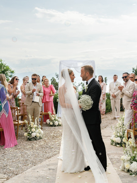 Newly married couple embracing beneath the ceremony arch at Pyrgos Ralli in Aegina