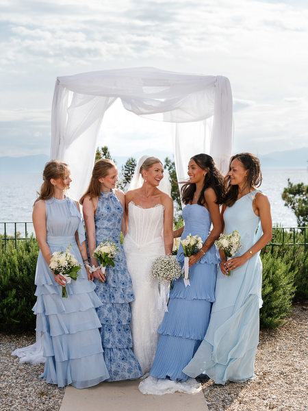 Bride posing with bridesmaids in blue dresses beneath the white ceremony arch