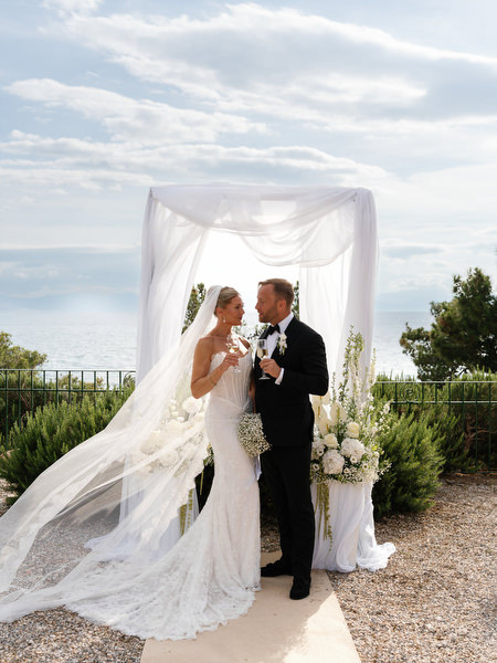 Bride and groom kissing beneath the ceremony arch with her veil blowing in the breeze