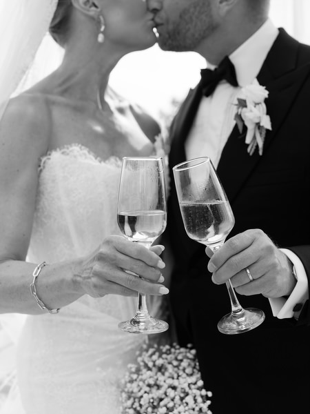 Black and white close-up of the newlyweds sharing a kiss and holding champagne glasses